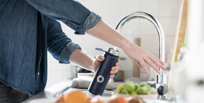 person filling up water bottle at kitchen sink