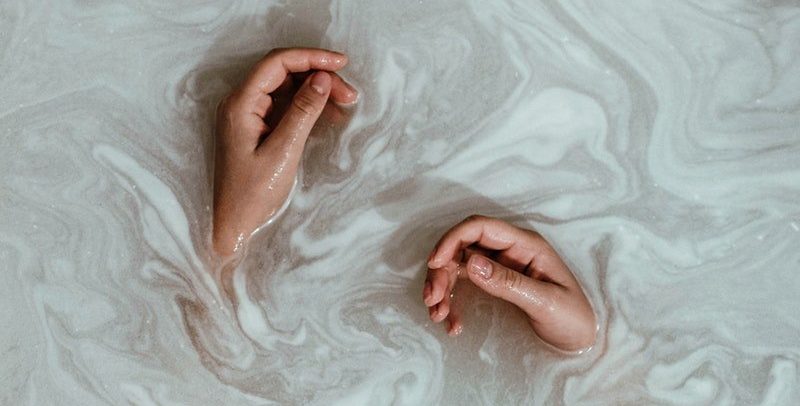 two hands in cloudy white bath bomb water