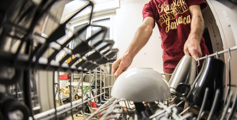 Fisheye image from inside dishwasher of man removing a small number of dishes from machine