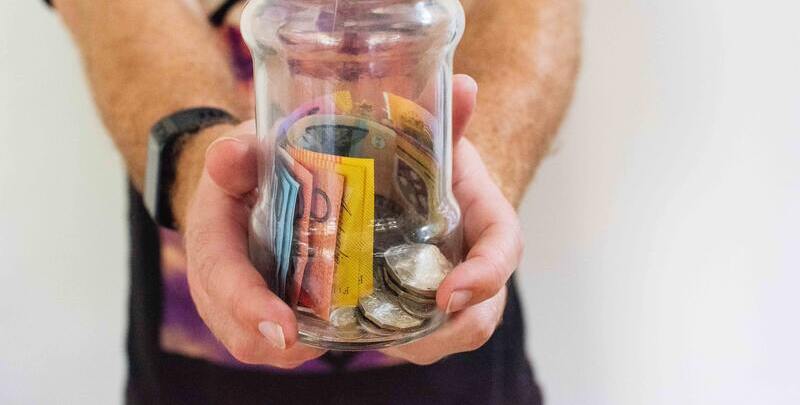 Male hands holding a glass jar of Australian currency notes and coins.