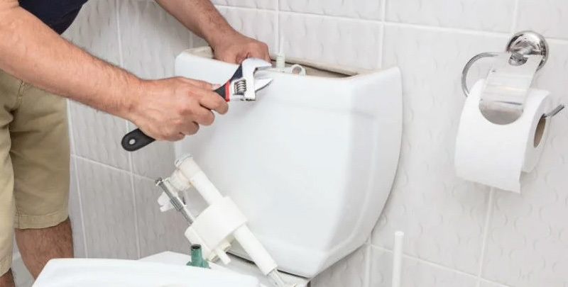 A plumber works on a toilet cistern