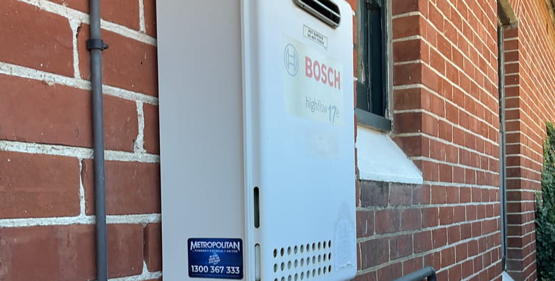 Bosch instant hot water system installed on outside wall of red bricked home. 